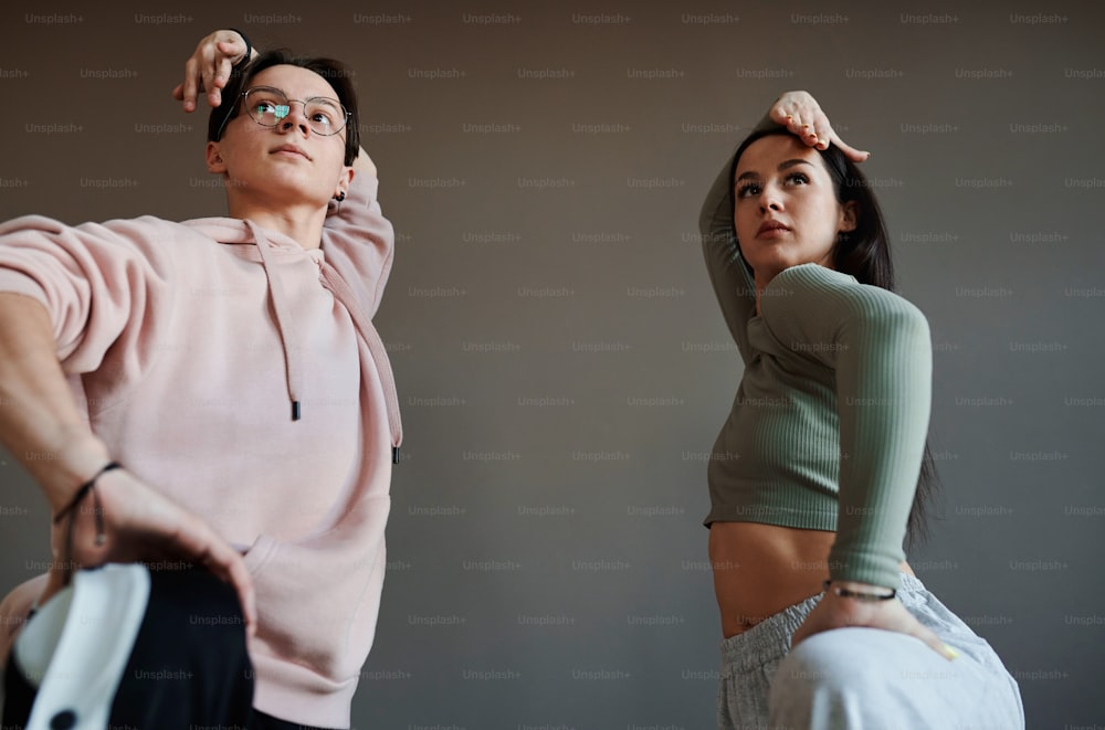 두 명의 활동적인 십대들이 현대 스튜디오나 댄스홀에서 유행 춤의 새로운 동작을 훈련하는 동안 머리 위로 팔을 들고 있습니다