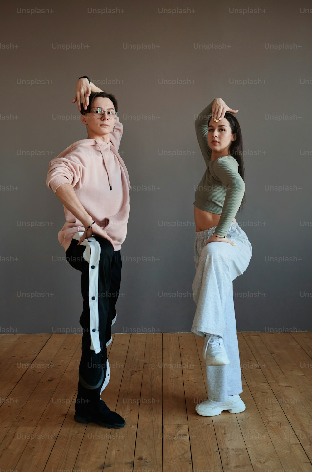 Dois jovens dançarinos da moda em roupas ativas mantendo as pernas dobradas no joelho enquanto trabalham em novos movimentos durante o treinamento em estúdio