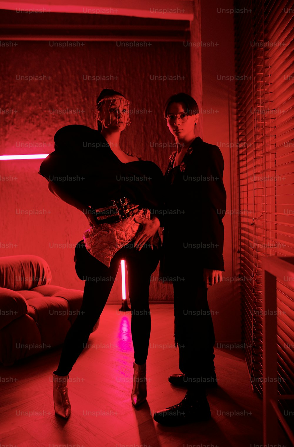 Young couple of vogue dancers in stage apparel standing in front of camera in studio lit with red light and neon lamps