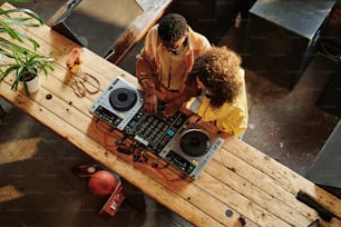 Above view of young intercultural couple in casualwear creating new music while guy showing his girlfriend how to mix sounds