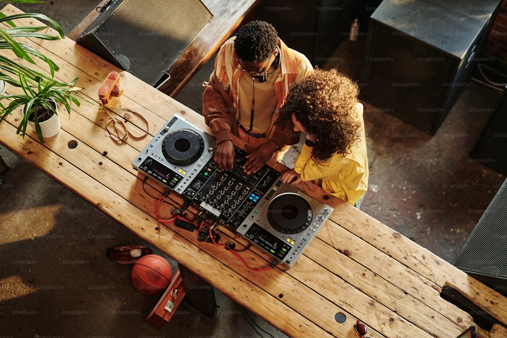Vista de una joven pareja intercultural en ropa casual creando nueva música mientras el chico le muestra a su novia cómo mezclar sonidos