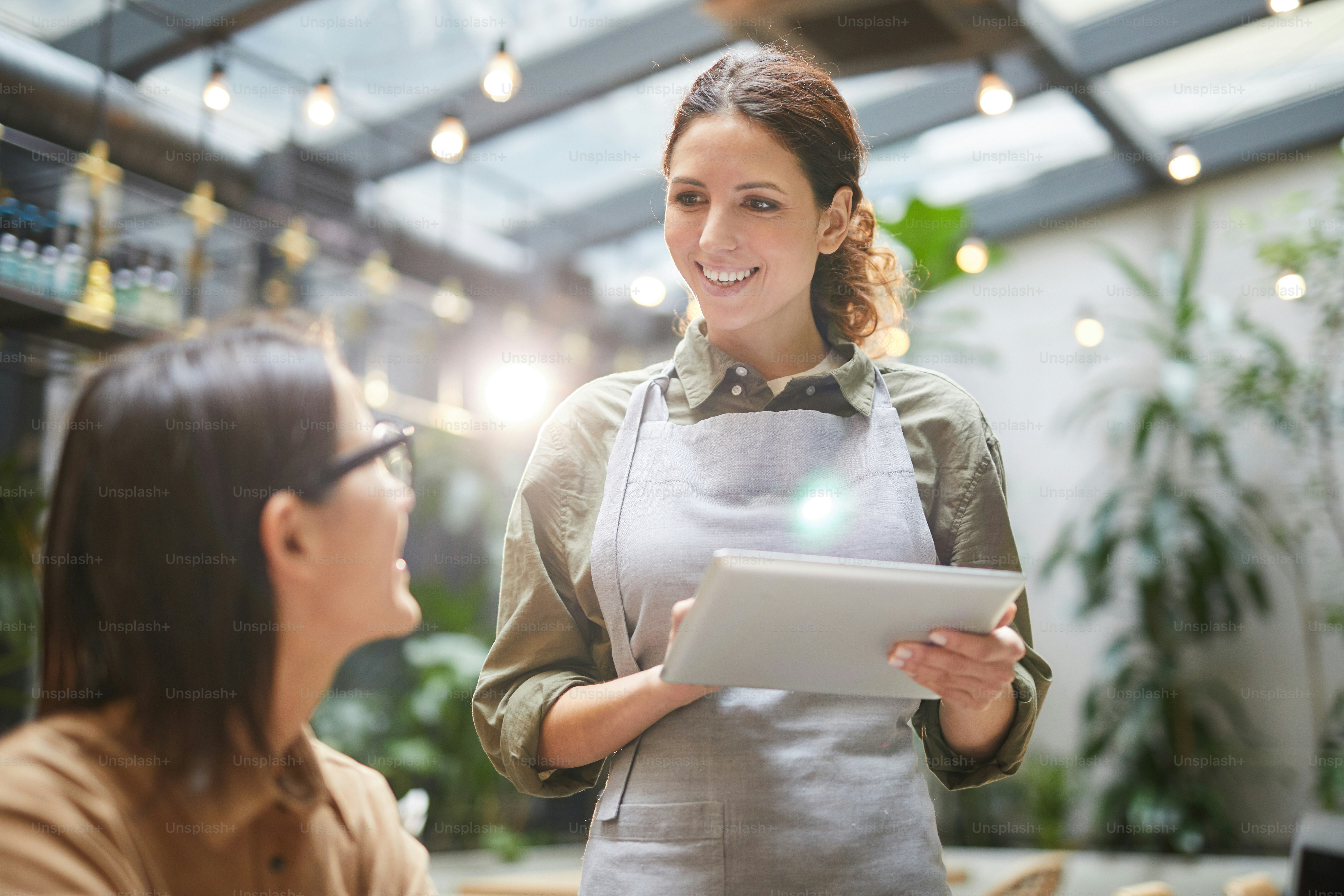 Waist up portrait of young waitress holding digital tablet while taking order of client at outdoor cafe terrace, copy space