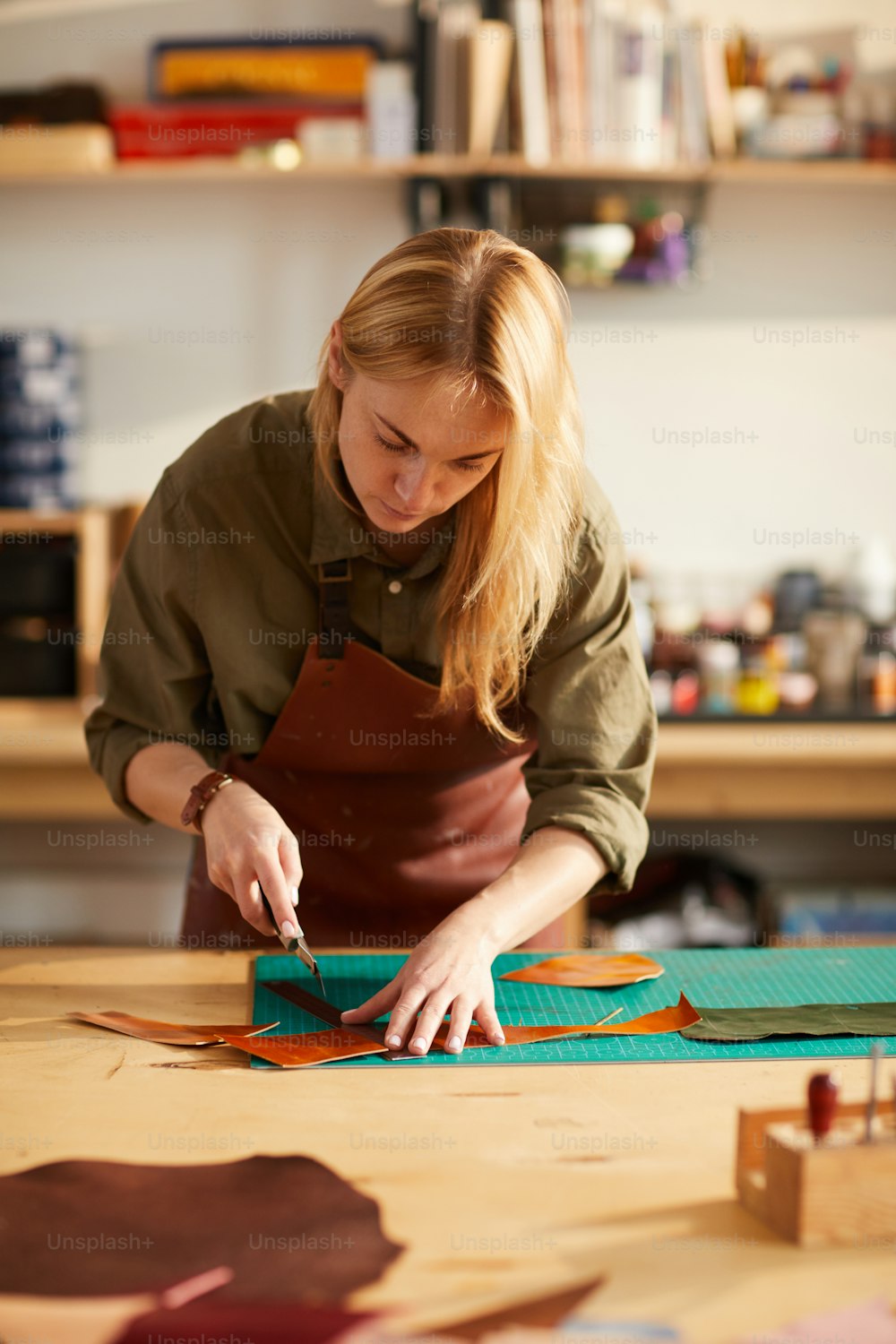 Retrato da mulher nova que corta os padrões de couro na oficina do atelier, espaço da cópia