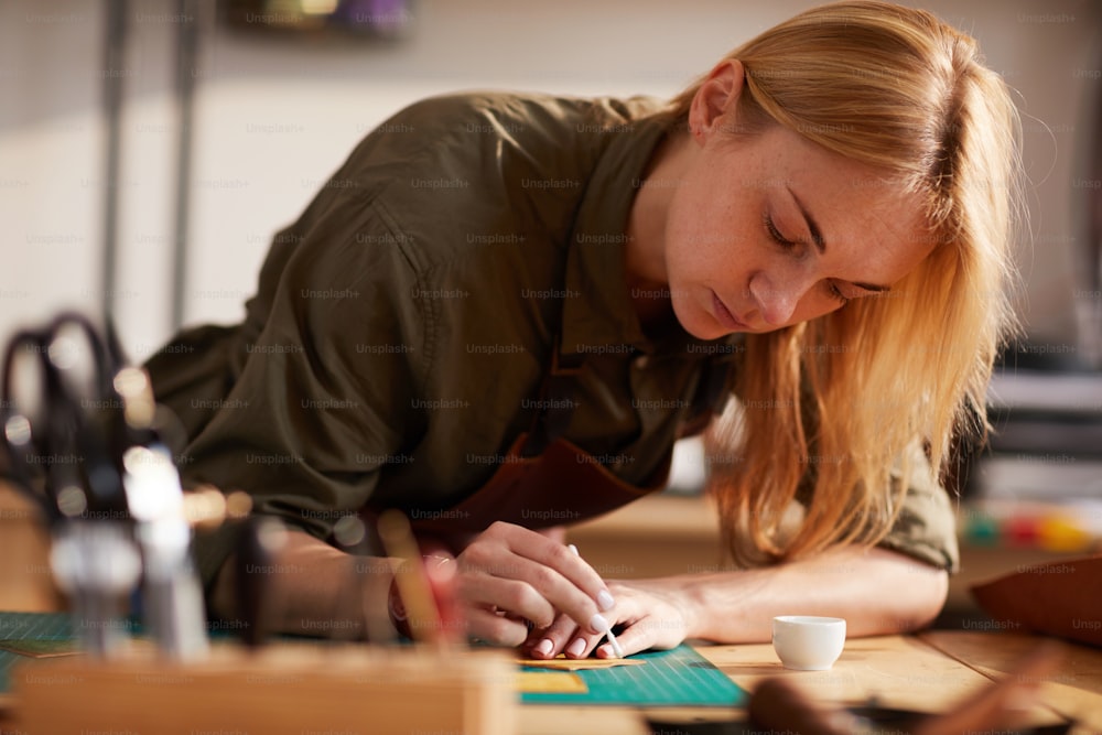 Warmes Porträt einer jungen Frau, die Ledermuster nachzeichnet, während sie in einem Schuhatelier arbeitet