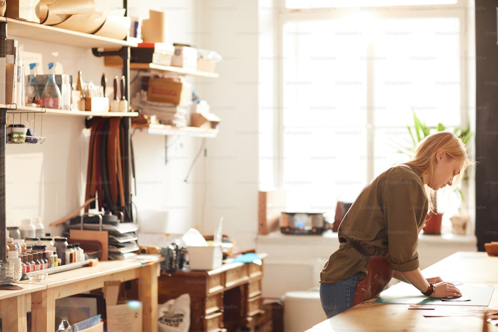 Side view portrait of young woman working in artisan workshop lit by sunlight, copy space