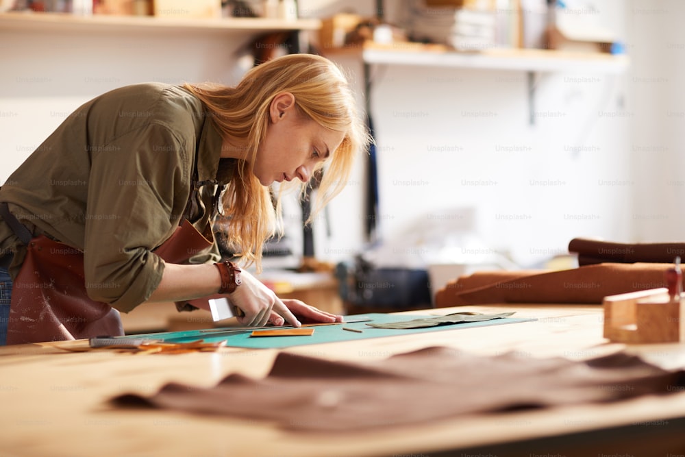 Vue latérale portrait d’une jeune femme découpant des motifs en cuir dans l’atelier atelier, espace de copie