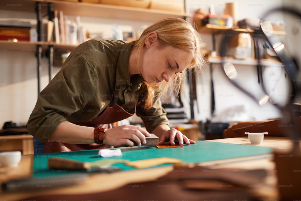 Warmes Porträt einer Kunsthandwerkerin, die Ledermuster nachzeichnet, während sie im Schuhatelier und im Kopierraum arbeitet