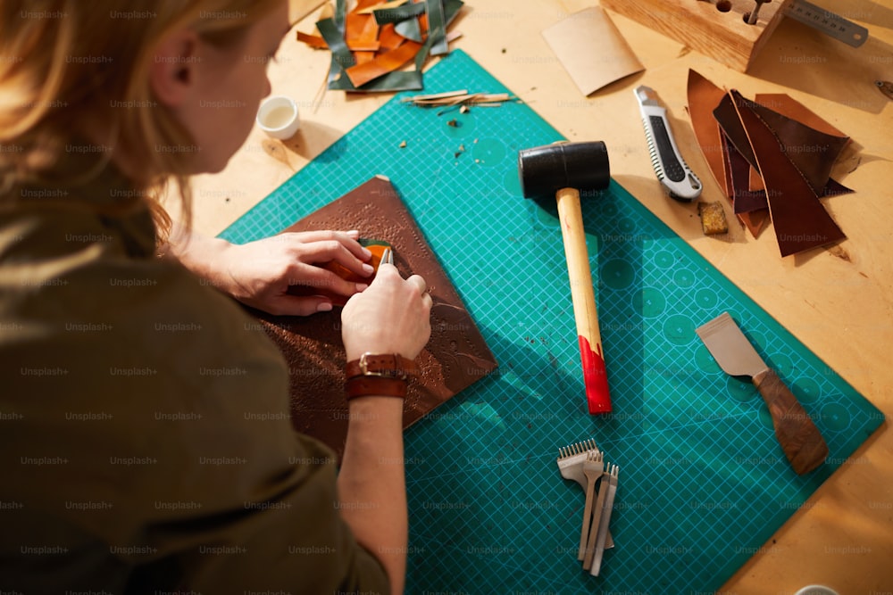 Hochwinkelporträt einer Kunsthandwerkerin, die Ledertasche in einem vom Sonnenlicht beleuchteten Atelier herstellt, Kopierraum