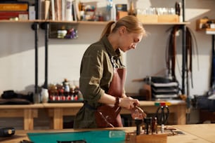 Seitenansichtsporträt einer Handwerkerin, die mit Leder in einer von Sonnenlicht beleuchteten Gerberei arbeitet, Kopierraum