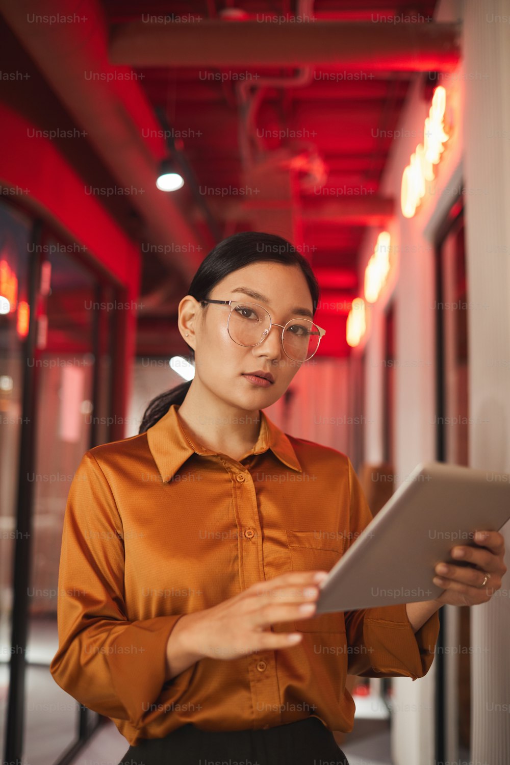 Retrato de cintura para arriba de una mujer de negocios asiática moderna sosteniendo una tableta y mirando a la cámara mientras posa al aire libre