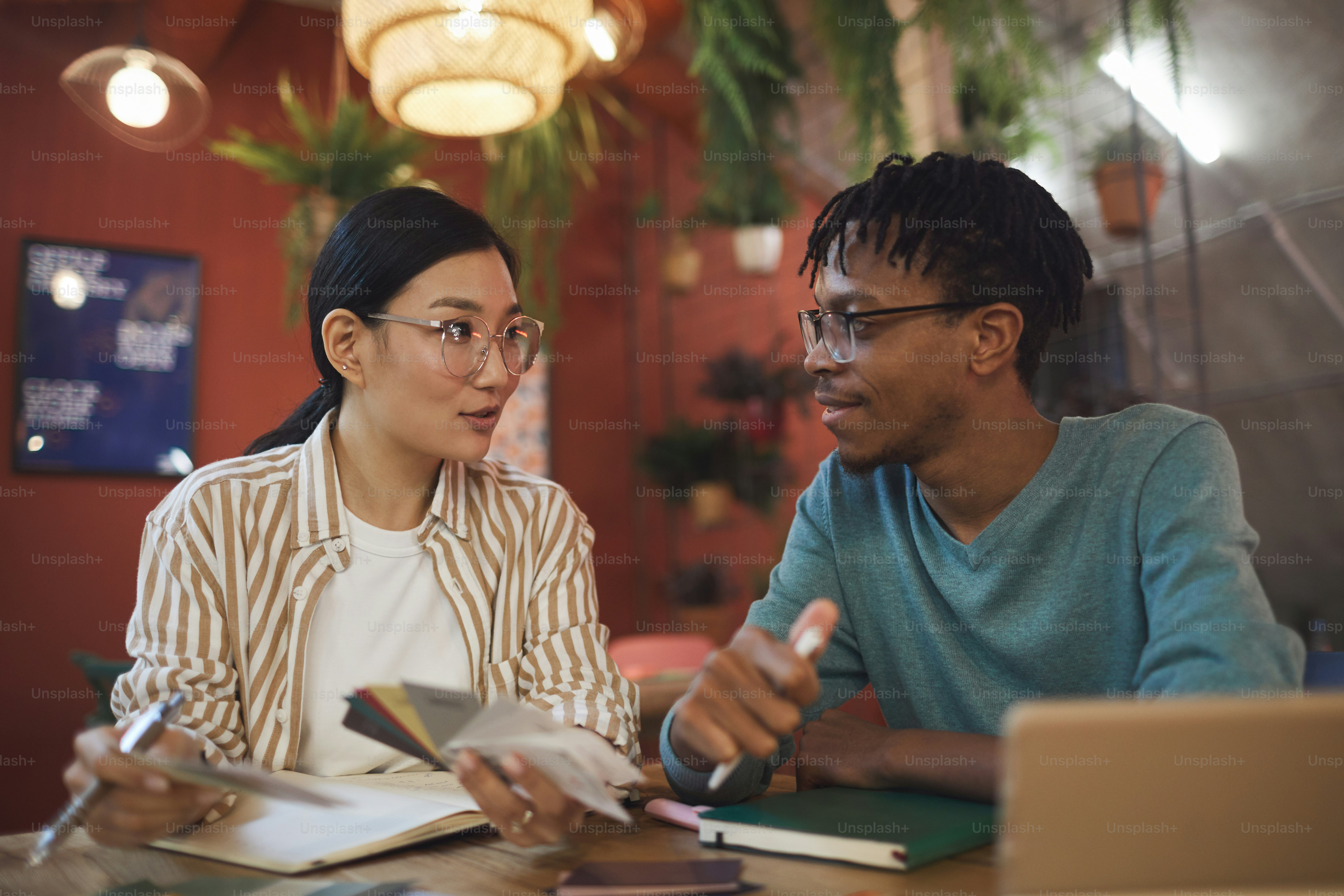 Portrait of two contemporary students working on project together while sitting at table in cafe