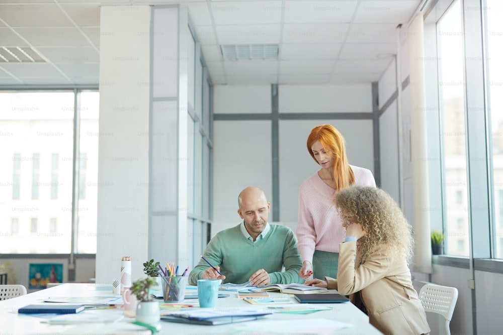 Group of three business people discussing documents while working at table in office, copy space