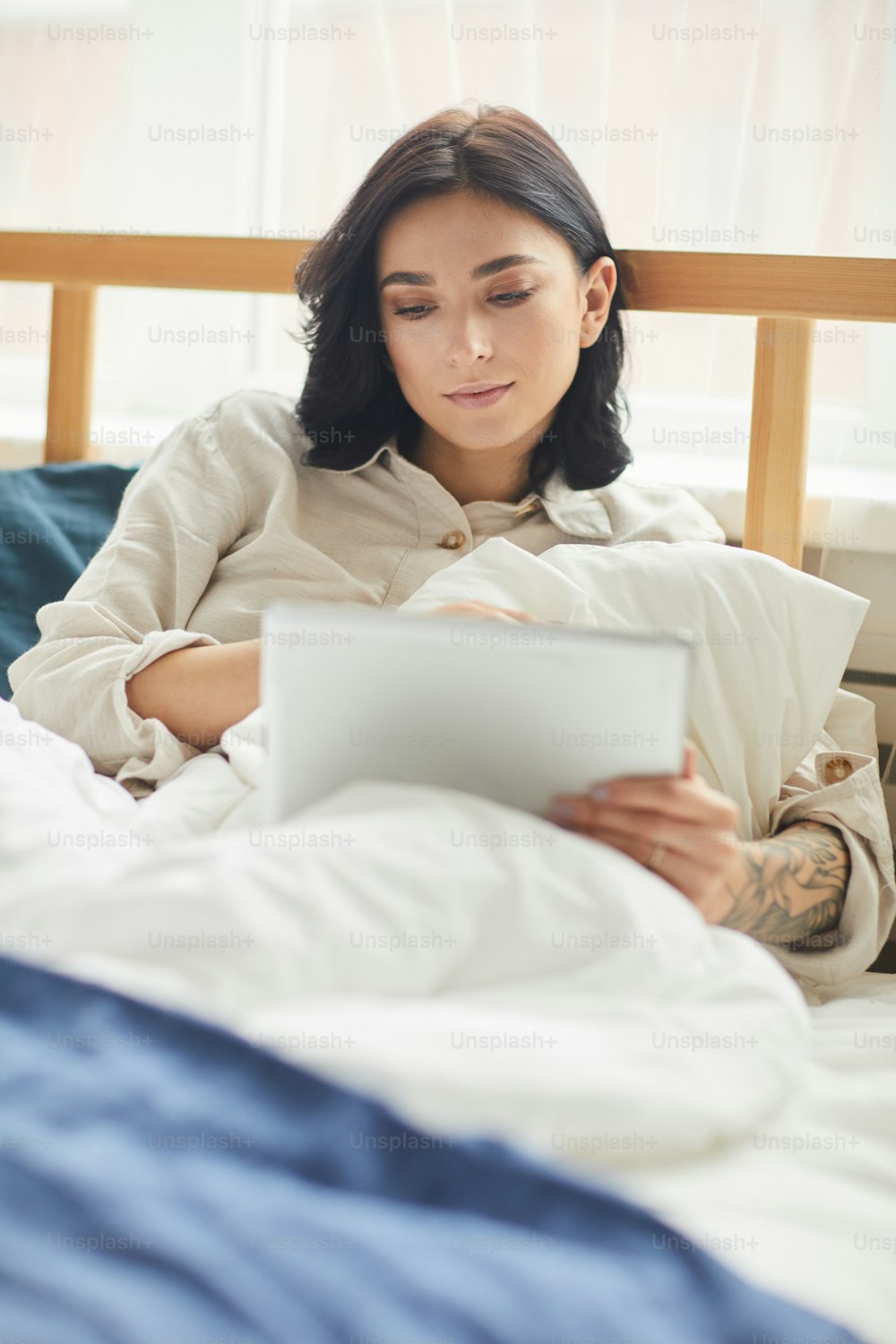 Retrato vertical da mulher adulta moderna usando tablet digital e navegando na internet enquanto deitado na cama confortável pela manhã, espaço de cópia