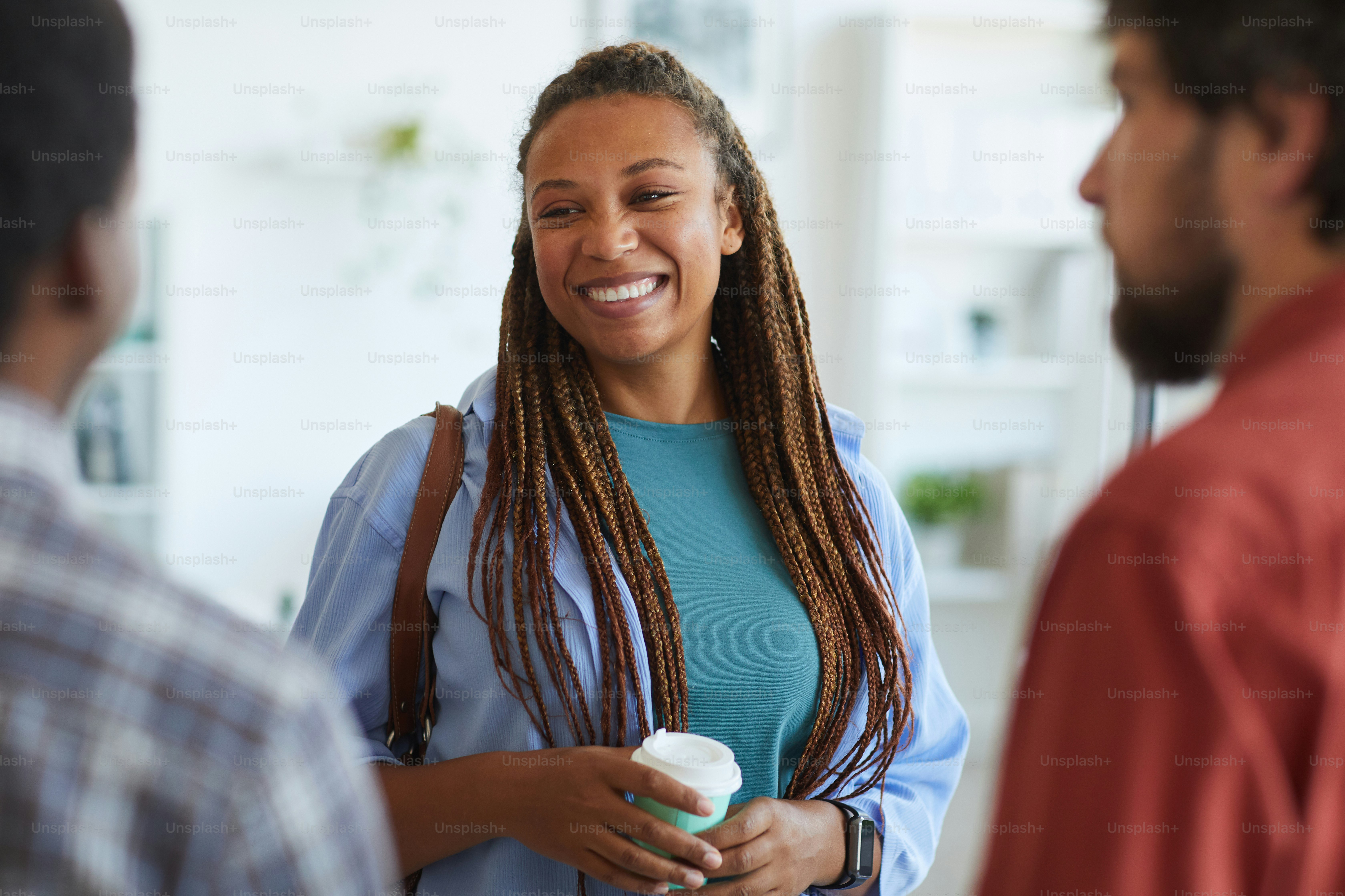 Retrato da cintura para cima da mulher afro-americana contemporânea sorrindo alegremente enquanto conversava com amigos ou colegas dentro de casa, espaço de cópia