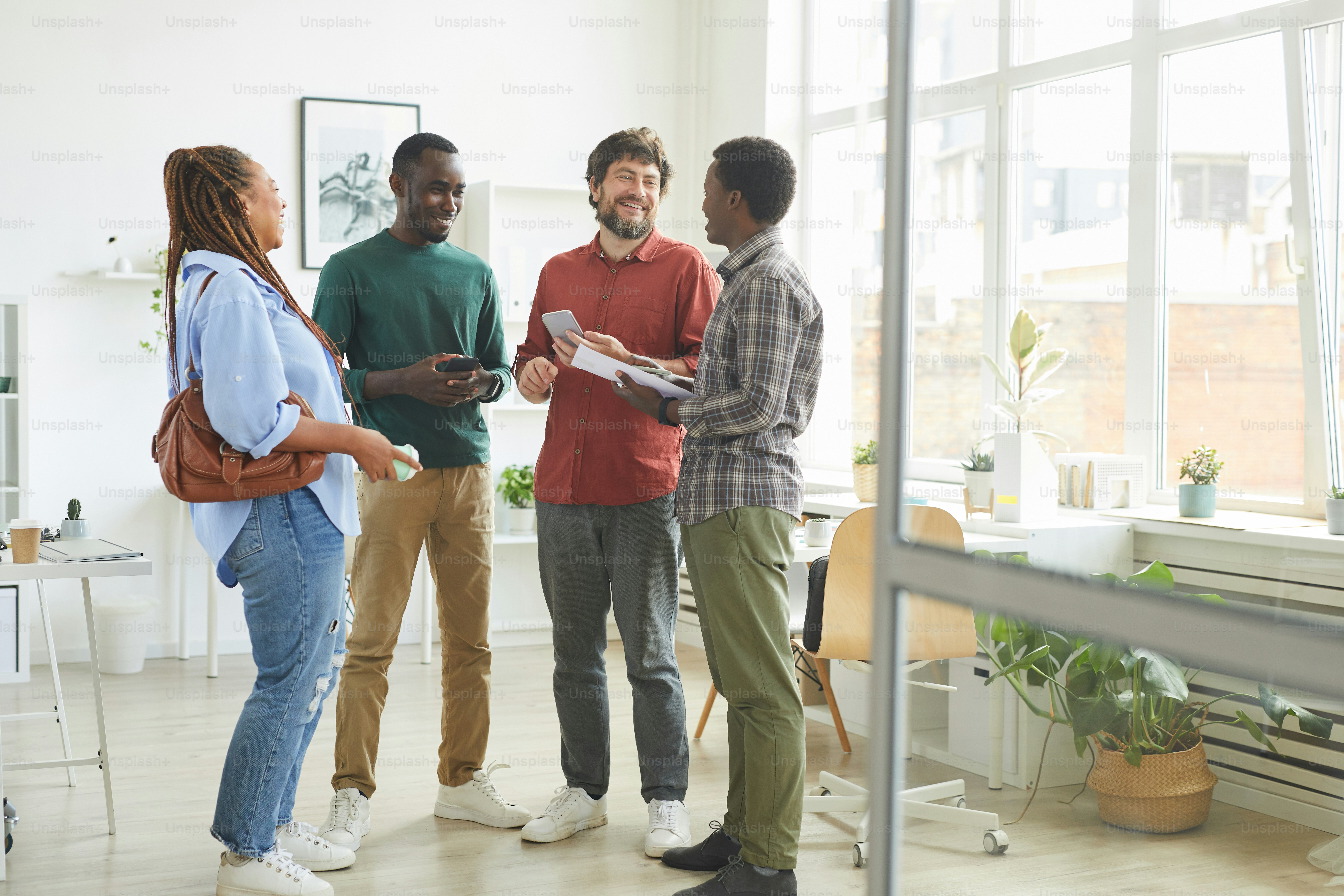 Retrato de corpo inteiro de um grupo multiétnico de pessoas vestidas com roupas casuais e sorrindo alegremente enquanto discutiam o trabalho em pé no cargo