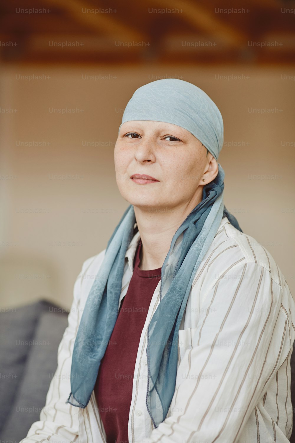 머리 스카프를 두른 대머리 성인 여성이 카메라를 바라보며 최소한의 홈 인테리어, 탈모증과 암 인식, 복사 공간에서 포즈를 취하는 세로 웜톤 초상화
