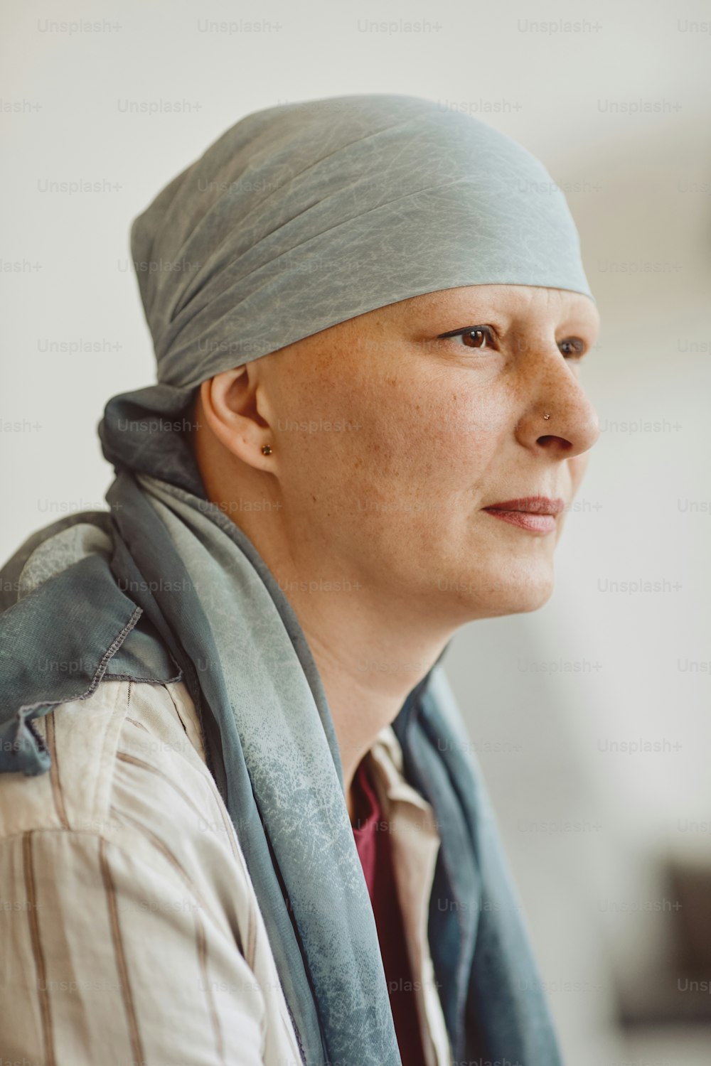 スカーフをかぶって物思いにふけって目をそらす禿げた成人女性の垂直側面図のポートレート、最小限の頭と肩のショット、脱毛症と癌の認識、コピー用スペース