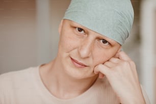 Warm-toned head and shoulders portrait of mature bald woman wearing headscarf and looking at camera pensively , alopecia and cancer awareness, copy space
