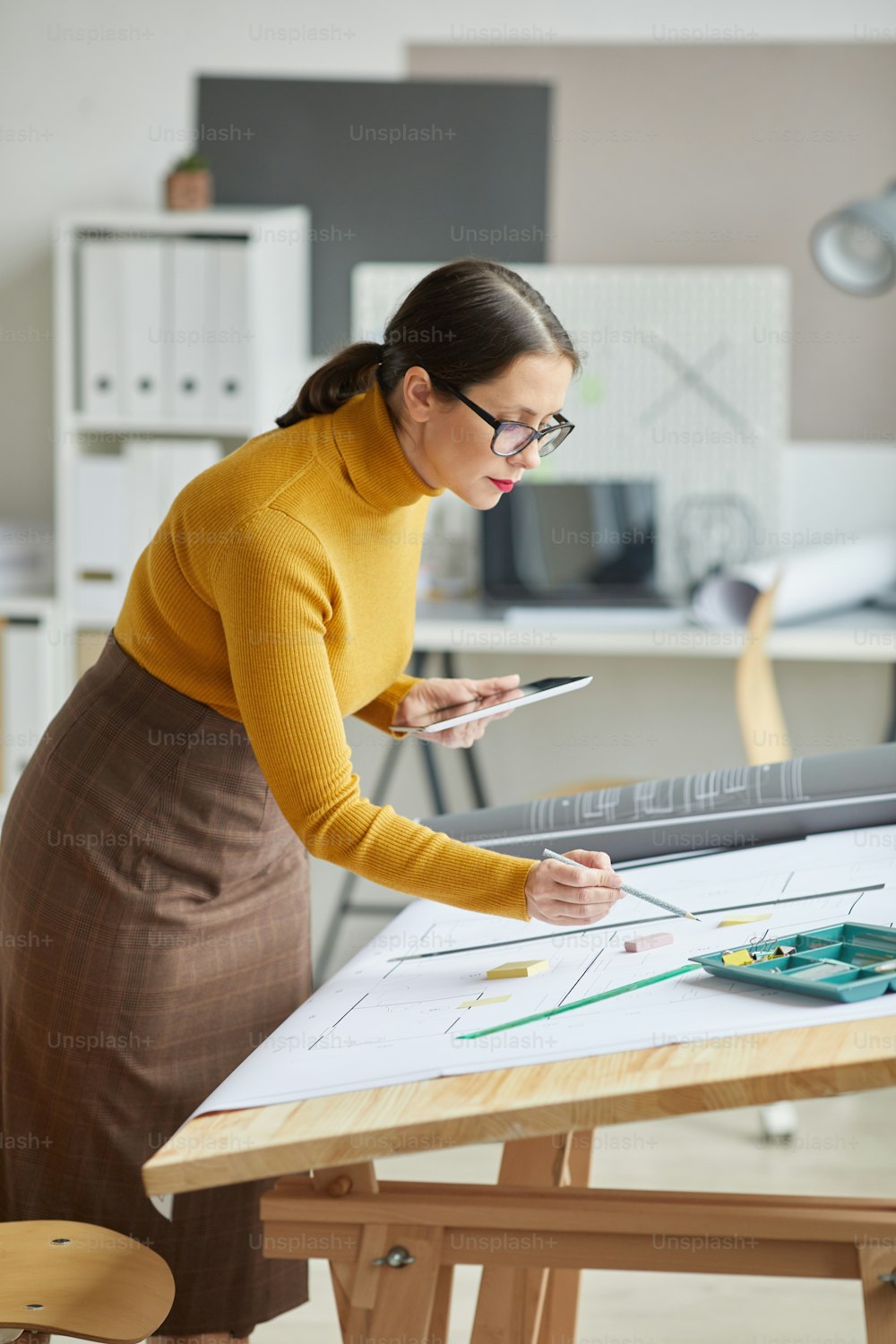 Vertikales Porträt einer Architektin, die Blaupausen zeichnet, während sie am Schreibtisch im Büro arbeitet, Kopierraum