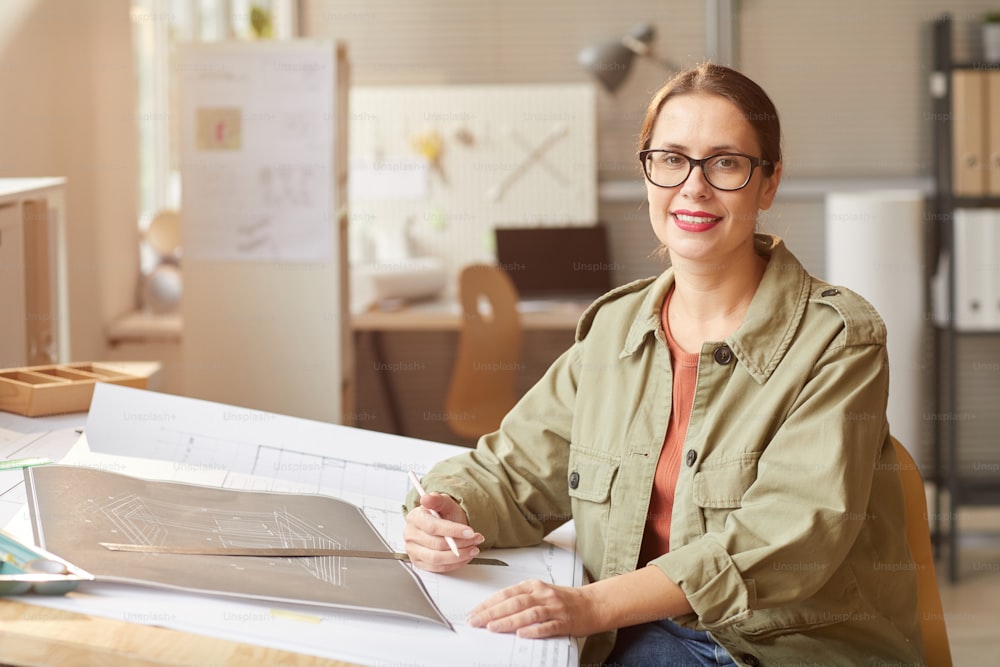 Portrait d’une jeune femme souriante dessinant des plans et des plans tout en travaillant au bureau dans le bureau des ingénieurs, espace de copie