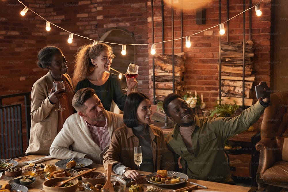 Multi-ethnic group of cheerful adult people taking selfie photo while enjoying party with outdoor lighting
