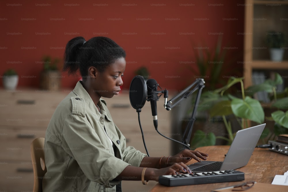 Side view portrait of young African-American woman composing music in home recording studio, copy space