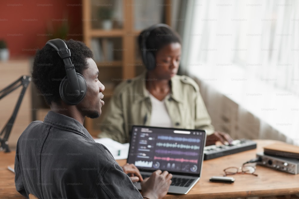 Vista de perfil en un joven músico afroamericano con auriculares mientras compone música en el estudio de grabación de casa, espacio de copia