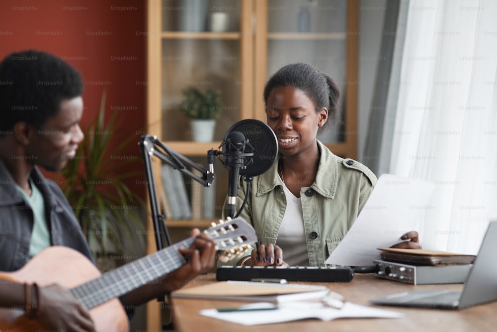 Portrait of young African-American woman singing to microphone while recording music in home studio, copy space
