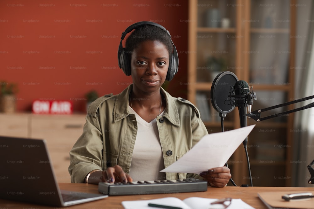 Portrait of smiling African-American woman looking at camera and wearing headphones while composing music in recording studio, copy space