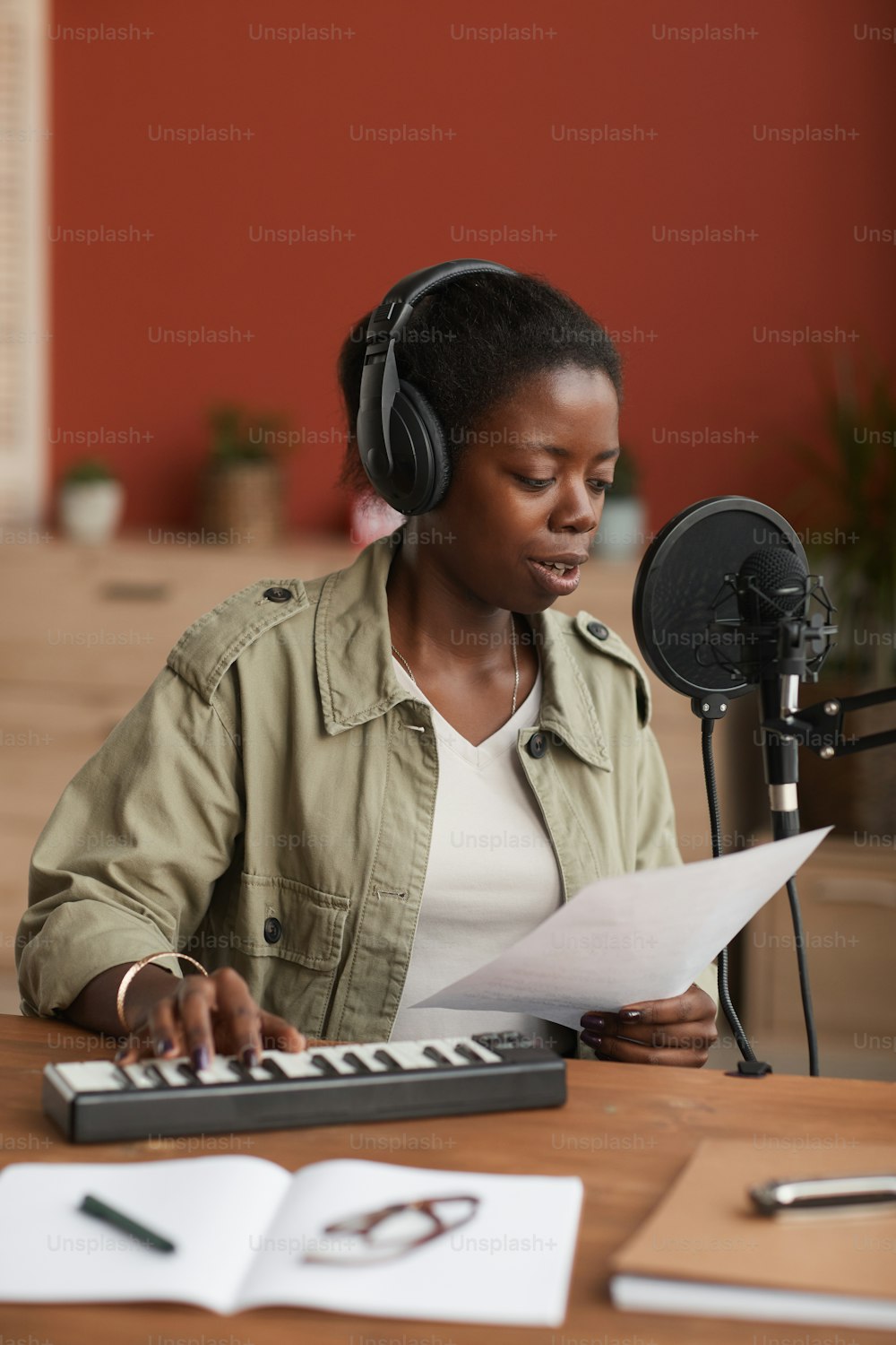 Vertical portrait of young African-American woman composing music and singing to microphone in home recording studio
