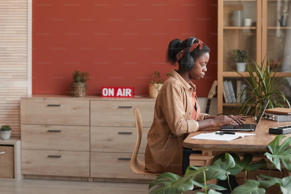 Retrato de vista lateral de una músico afroamericana usando una computadora portátil mientras compone música en casa, espacio de copia