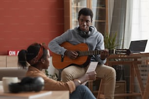 Retrato de dos jóvenes músicos afroamericanos tocando la guitarra y escribiendo música juntos en un estudio de grabación casero
