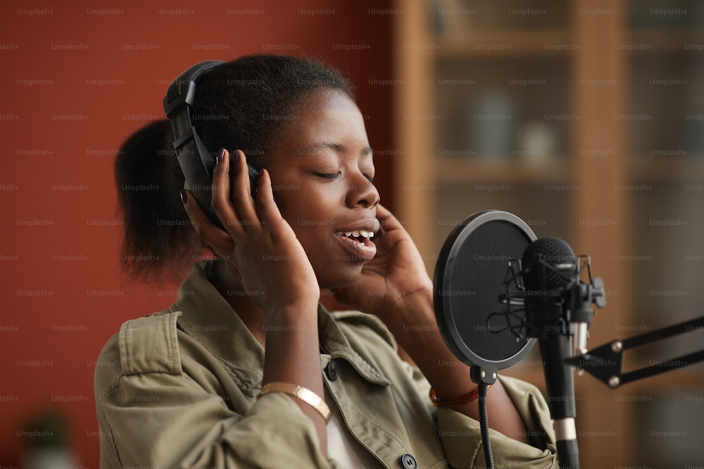 Porträt einer talentierten afroamerikanischen Frau, die zum Mikrofon singt und Kopfhörer trägt, während sie Musik im Studio und im Kopierraum aufnimmt