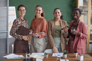 Multi-ethnic group of smiling contemporary businesswomen looking at camera while standing in office