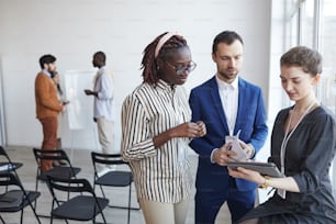 Cintura para cima retrato de grupo multi-étnico de jovens discutindo o trabalho enquanto olha para tablet na sala de conferências, espaço de cópia