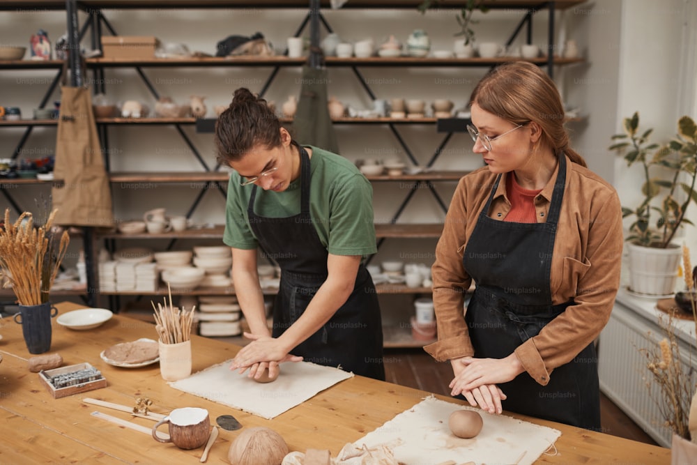 Portrait of two young people shaping clay while making ceramics in pottery workshop, hobby and small business concept, copy space