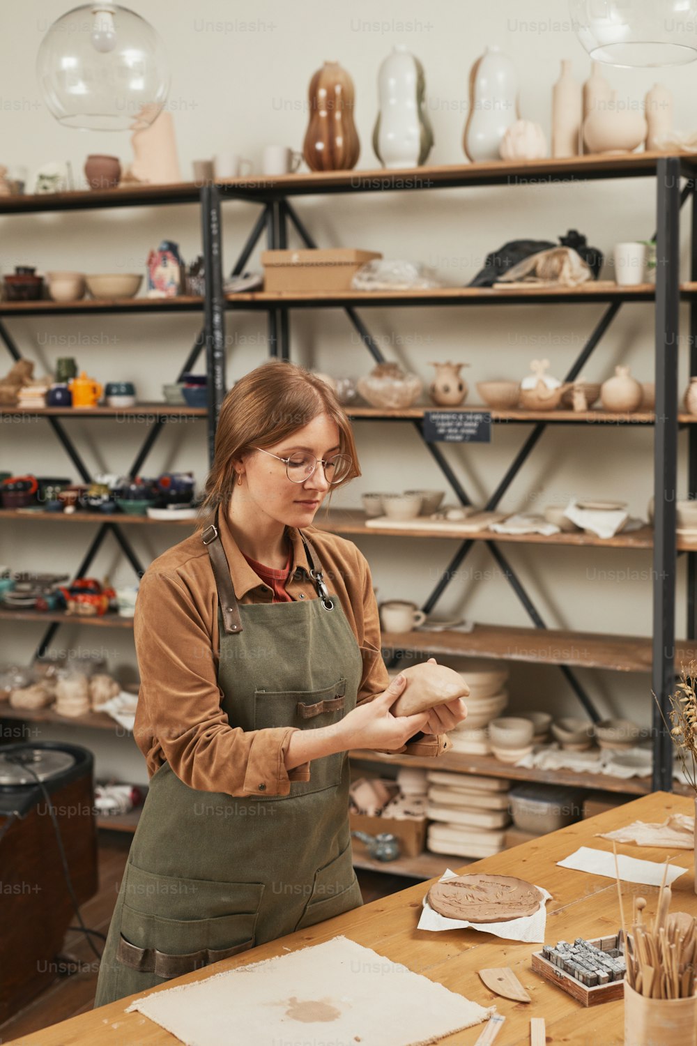 Retrato vertical de tonos cálidos de una mujer joven dando forma a la arcilla mientras hace cerámica en un taller de cerámica, concepto de pequeña empresa, espacio de copia