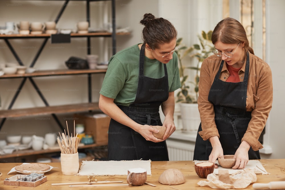 Retrato en tonos cálidos de dos jóvenes dando forma a la arcilla mientras hacen cerámica en un taller de cerámica, hobby y concepto de pequeña empresa, espacio de copia