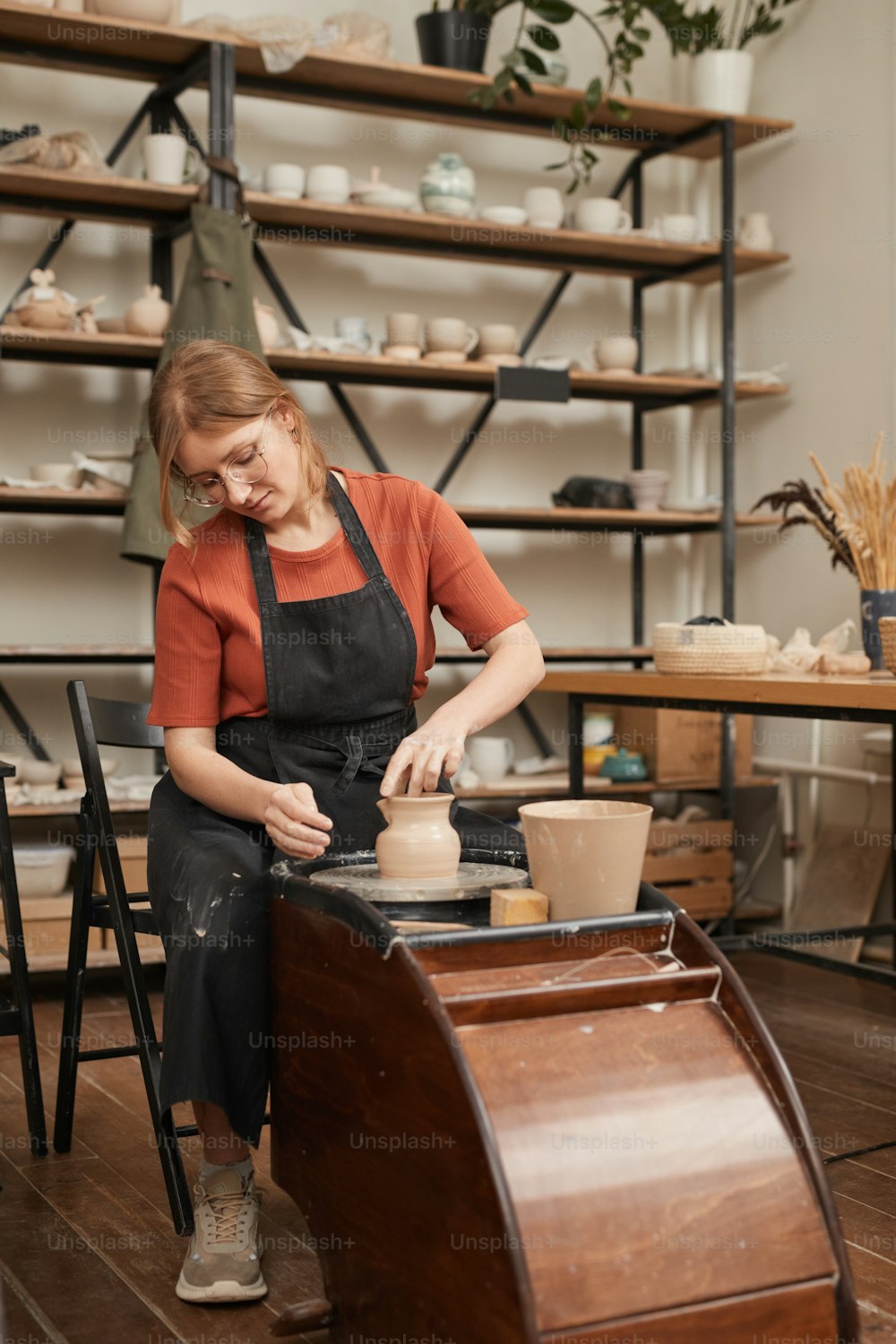 Retrato vertical de tonos cálidos de una joven alfarera dando forma a arcilla en cerámica mientras hace cerámica en el taller y disfruta de las artes y manualidades