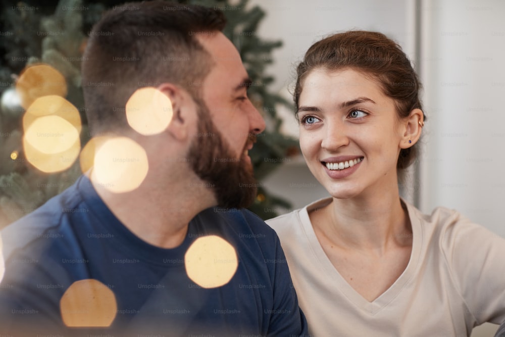 Feliz joven mujer caucásica mirando con amor a su novio mientras celebran la Navidad juntos, destello de lente