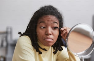 Portrait en gros plan d’une vraie femme afro-américaine se maquillant tout en se regardant dans un miroir, focus sur les imperfections de la peau, espace de copie