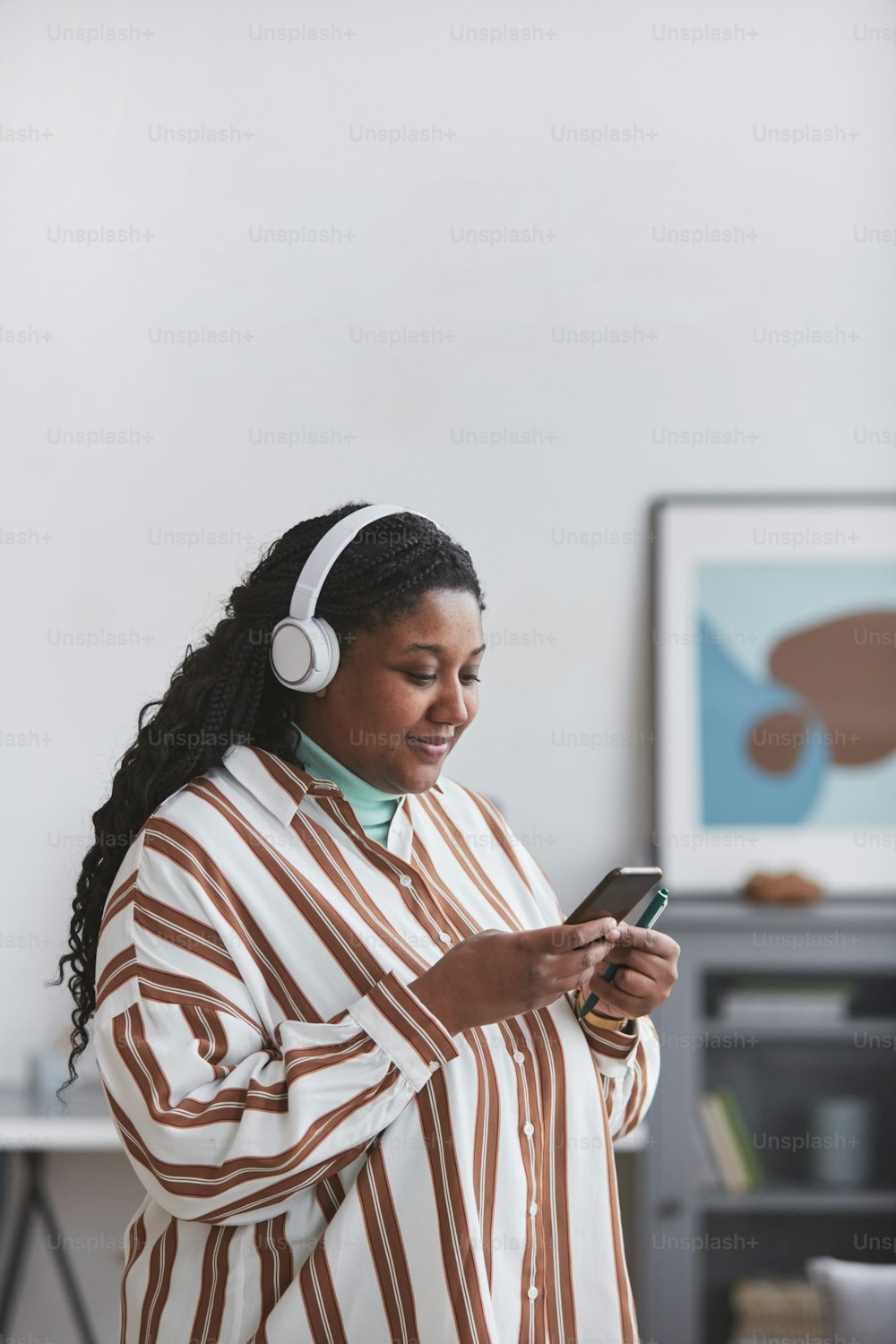 Minimales Porträt einer kurvigen Afroamerikanerin, die Kopfhörer trägt und Musik über das Smartphone in hellem Wohnraum genießt