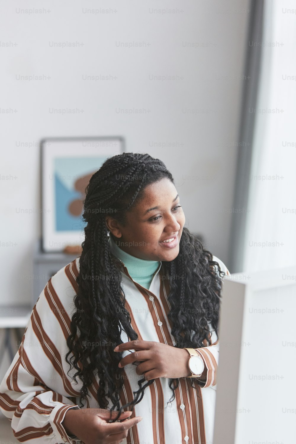 Vertical portrait of curvy African-American woman looking in mirror and smiling happily while enjoying dressing up at home