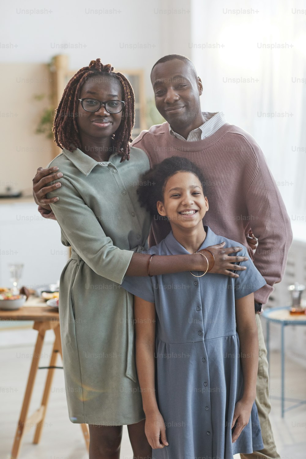 Vertical portrait of happy African-American family looking at camera while posing indoors in cozy home interior with dinner table in background