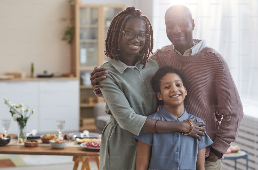 Portrait of happy African-American family looking at camera while posing indoors in cozy home interior with dinner table in background, copy space