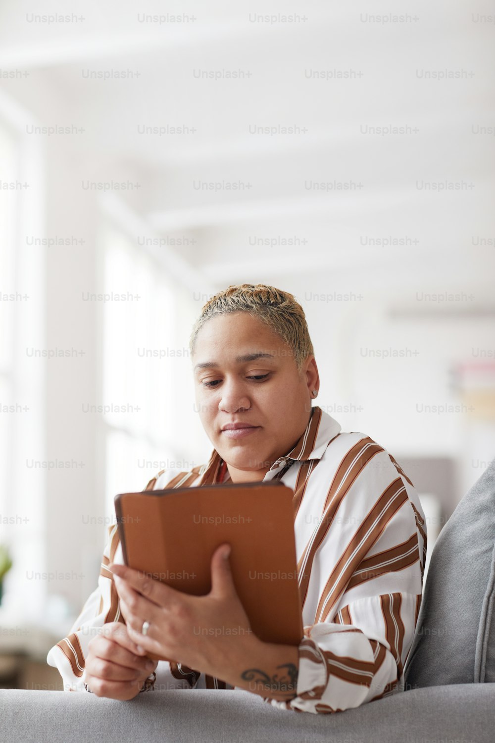 Vertikales Porträt einer modernen gemischtrassigen Frau, die ein digitales Tablet hält, während sie die Online-App zu Hause verwendet.
