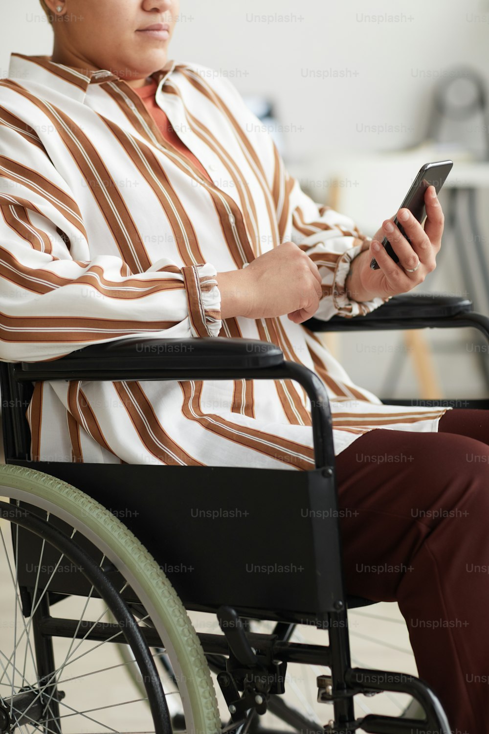 휠체어에 앉아 있는 동안 스마트폰을 사용하는 현대 장애인 여성의 자른 세로 초상화
