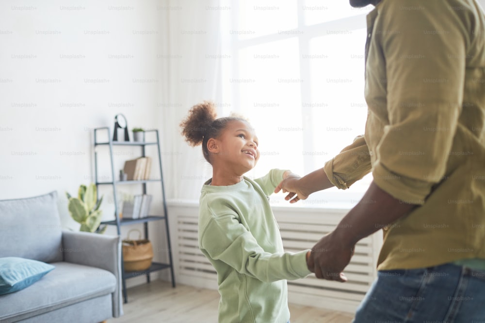 Portrait of cute African-American girl dancing with father in minimal home interior, copy space