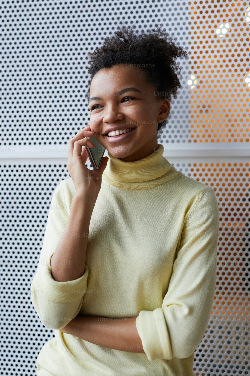 Vertical waist up portrait of young African-American woman speaking by smartphone and smiling cheerfully