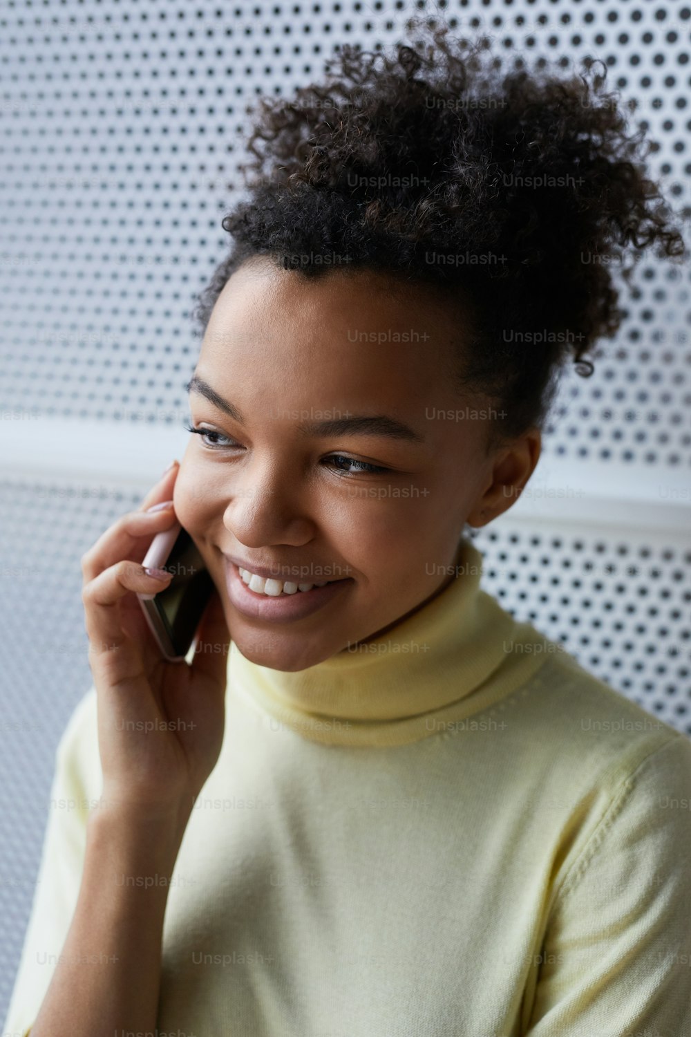 Ritratto verticale ravvicinato di giovane donna afroamericana che parla con lo smartphone e sorride allegramente
